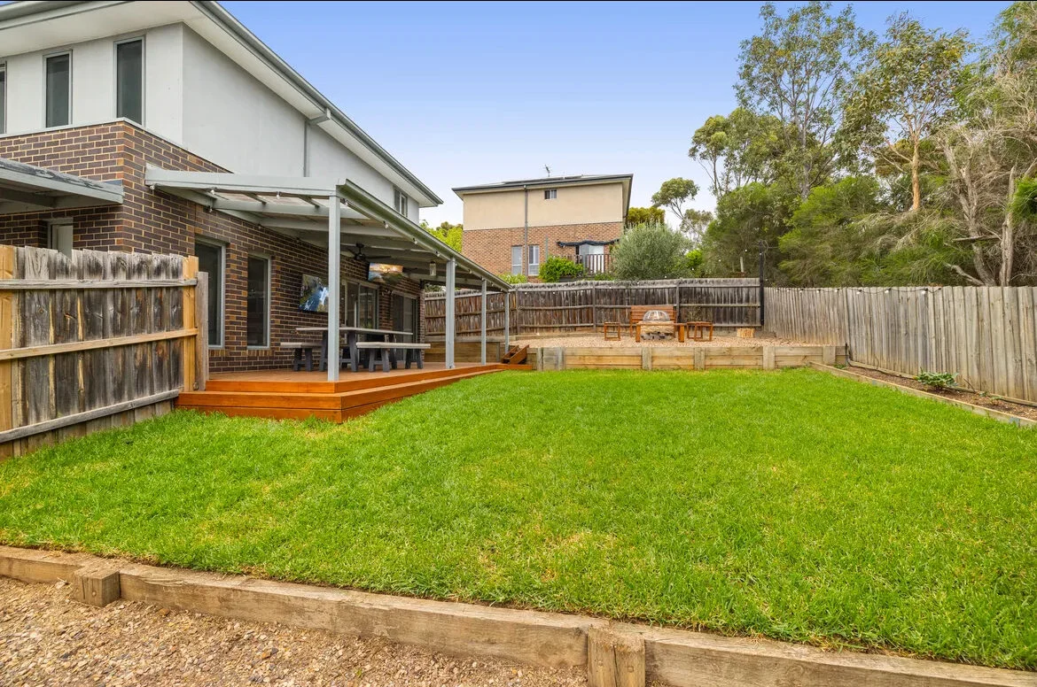 Green lawn turf in a modern residential backyard with timber retaining walls and outdoor patio in Melbourne.
